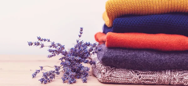 Home wardrobe with winter clothes. Woolen sweaters and dried lavender for protection from moth. Knitted warm wool clothes. Stack of warm knitted clothes with lavender. Autumn, winter season knitwear.