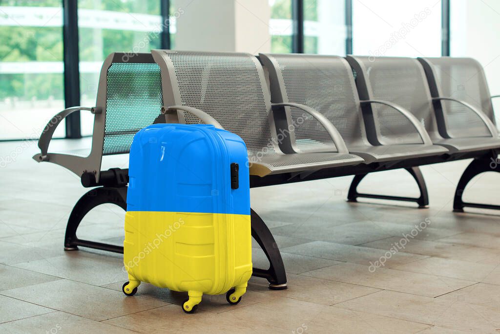 A large blue and yellow suitcase on wheels sits on the floor in a modern airport terminal. Ukrainian refugees are leaving the country.