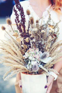 Çiçek sonbahar kompozisyonu. Kurumuş bitkiler, çiçekler ve sonbahar yaprakları. Çiçeksel sanat dekorasyonu. Sonbahar tatili için elinde şık bir çiçek bezi tutan bir kadın..