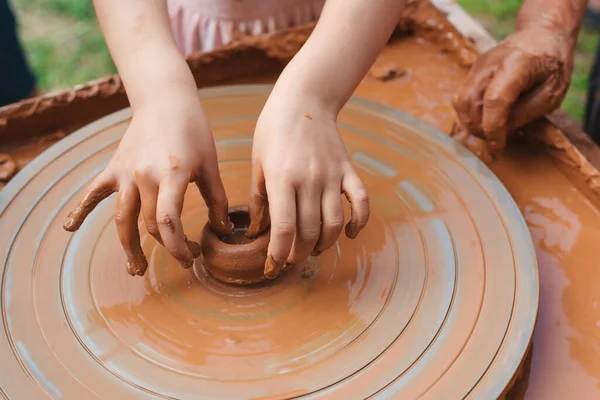 Teacher and kid making ceramic pot. Potters and child hands. Pottery workshop outside. Master teaching kid to creating on the pottery wheel. Grandmom teaches granddaughter pottery. Clay modeling.