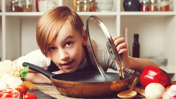 Child cooking. Cute little chef holding frying pan at kitchen. Funny boy wearing apron. Future profession. Chef trying a new recipe. Boy at cooking classes.