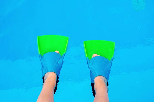 Kid legs with swim flippers over blue water background. Flippers in water. Diver fins. Underwater kids legs in fins in swimming pool, top view. Mockup with copy space.