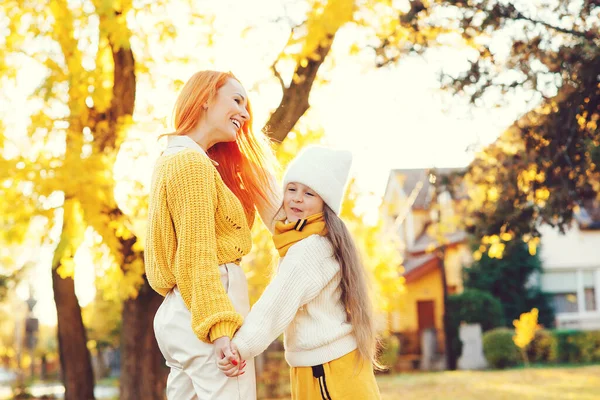 Happy family in autumn park. Mother and child daughter playing on autumn walk. Mom and girl laughing outdoors. Autumn fashion.