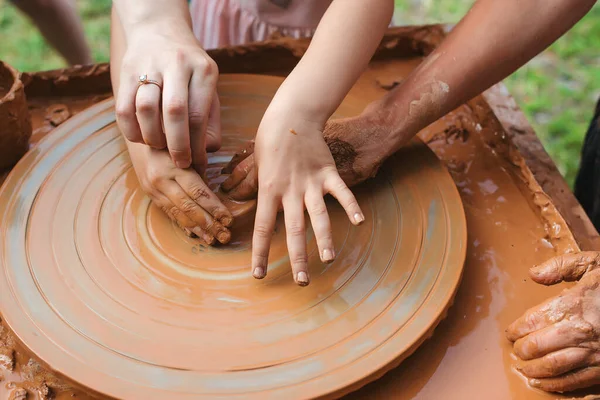 Teacher and kid making ceramic pot. Potters and child hands. Pottery workshop outside. Master teaching kid to creating on the pottery wheel. Grandmom teaches granddaughter pottery. Clay modeling.