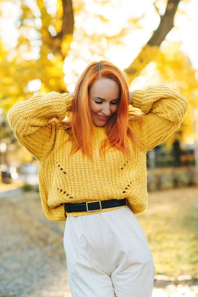 Pretty woman enjoying sunny autumn day. Autumn holidays. Girl wearing yellow sweater. Happy woman outdoor portrait. Redhead woman walking in autumn park. Autumn fashion and season.
