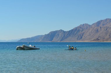 Uzak dağların arka planında kano süren bir aile.