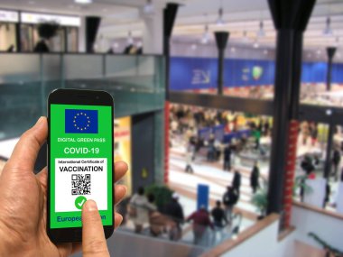 Alışveriş merkezinde elinde Covid-19 için Avrupa Birliği dijital yeşil kartı olan bir akıllı telefon tutan bir adam. Coronavirus ve Yeşil Geçit için güvenlik kavramı