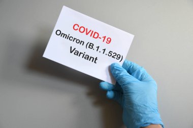 Doktorun elinde beyaz kağıtlı mavi eldiven ve Covid-19 Omicron Variant mesajı var. Tıbbi çeşitlilik Omicron ve COVID-19 kavramları. COVID-19 omikron varyant kavramı.