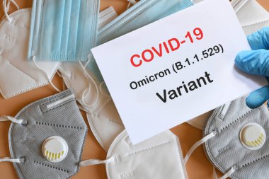 Doktorun elinde beyaz kağıtlı mavi eldiven ve arka planda çeşitli koruma maskeleri olan Covid-19 Omicron Variant mesajı var. COVID-19 omikron varyant türü koruma kavramı.