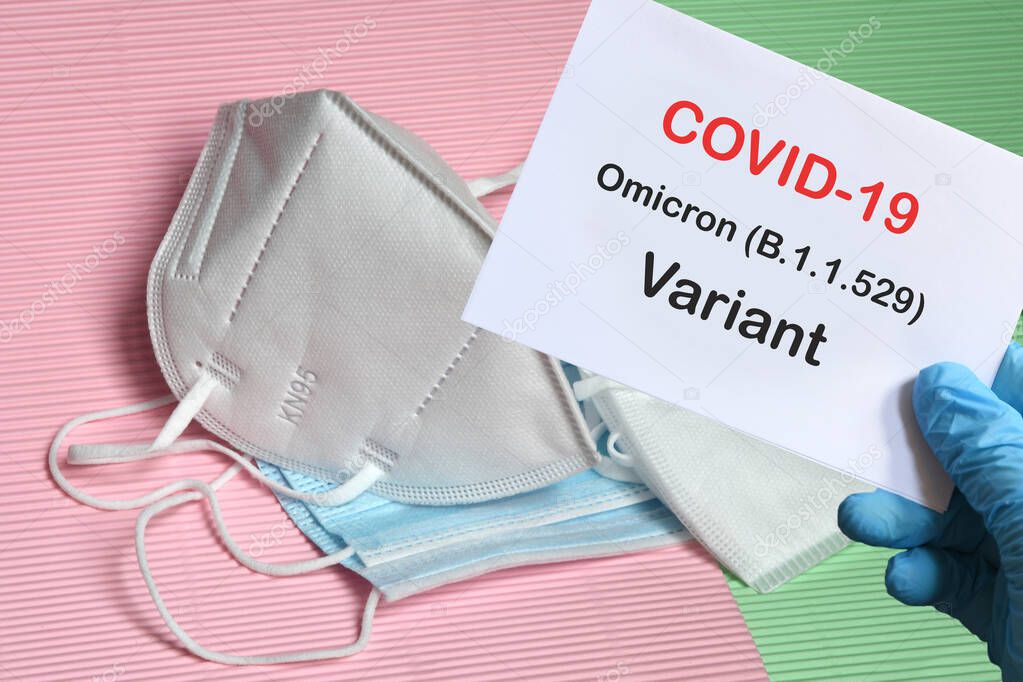 Doctor's hand in blue glove with white paper and text Covid-19 Omicron Variant with various protection masks on background. COVID-19 omicron variant strain protection concept.