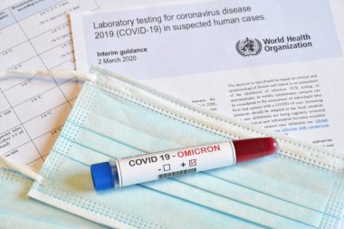 Florence, Aralık 2021: Covid 19 virüsünün yeni Omicron versiyonu. Tıbbi maske ve belgelerde pozitif Omicron COVID-19 kan örneği bulunan test tüpü. SARS-CoV-2 'nin yeni varyantı Omicron için koruma kavramı.