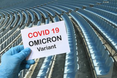 Covid 19 yeni Omicron versiyonu. Mavi eldivenli el boş tribünlerle dolu bir stadyumda üzerinde 