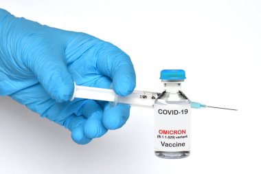 Mavi eldivenli doktor elinde Covid-19 virüsünün Omicron varyantı için bir şişe hipotetik aşı olan bir şırınga tutuyor..