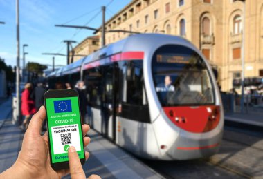 Tramvay durağındaki bir adam Avrupa Birliği dijital SARS-19 SARS-CoV-2 için yeşil geçiş kartı tutuyor. Koronavirüs salgını ve Yeşil Geçit sırasında güvenli seyahat kavramı.