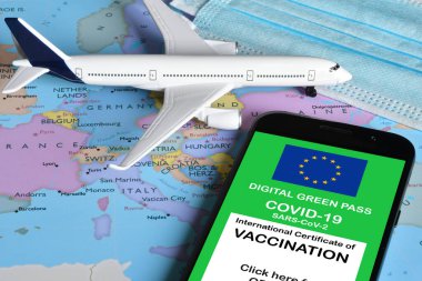 Traveling during the corona virus pandemic. Smartphone with european digital covid-19 vaccination certificate along with protective masks and airplane model on european map. Safe travel concept.