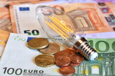 Avro banknotları ve bozuk paraları olan ampul. Pahalı enerji faturası ve artan elektrik fiyatları kavramı.