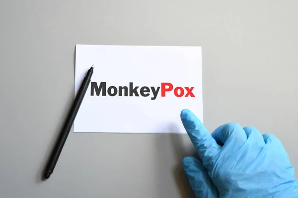 Doctor hand in blue glove with pen indicate Monkeypox words on white paper. Monkeypox on white paper. Monkeypox virus concept.