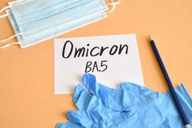 Koruyucu maskeler ve beyaz kağıtlı mavi ameliyat eldivenleri ve Omicron BA.5 Varyantı metni. Omicron Varyasyonu ve COVID-19 tıbbi çeşitlilik kavramı. COVID-19 Omicron BA.5 Değişken kavramı.