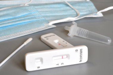 SARS-CoV-2 antigen test kit for self testing with negative result, one step coronavirus antigen rapid test, saliva swab with protection mask on background. close-up