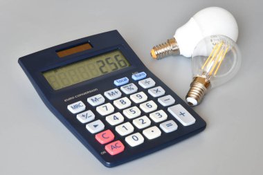 Gri arkaplanda ampuller ve hesap makinesi, yakın plan. Enerji fiyatlarına zam kavramı.