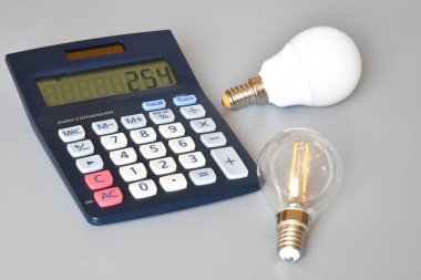 Gri arkaplanda ampuller ve hesap makinesi, yakın plan. Enerji fiyatlarına zam kavramı.