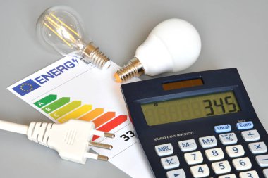 Gri arka planda ampulleri, hesap makineleri ve güç kablosu olan verimlilik derecelendirme tablosu, yakın plan. Enerji fiyatlarına zam kavramı.