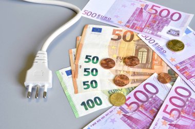 Avro para banknotlarıyla elektrik prizi ve gri arka planda sentler. Elektrik maliyetinin artması konsepti. Pahalı enerji faturası ve elektrik fiyatlarındaki artış.