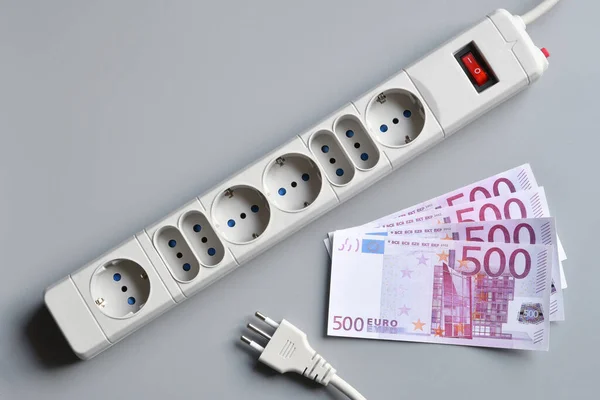 Euro banknotes with power plug of an extension socket on gray surface. Concept for the rising cost of electricity. Expensive energy bill and rising electricity prices.