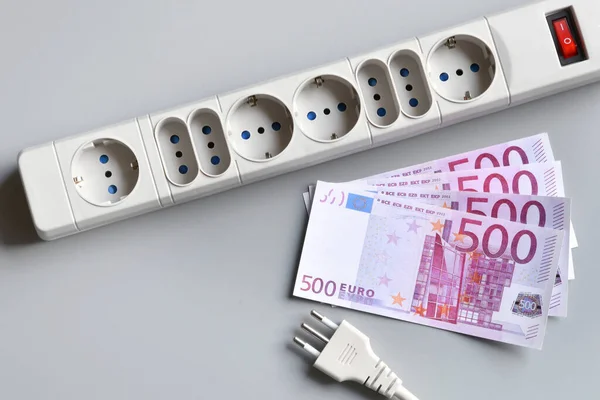 Euro banknotes with power plug of an extension socket on gray surface. Concept for the rising cost of electricity. Expensive energy bill and rising electricity prices.