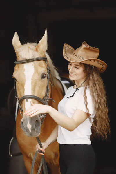 Portrait of rider woman in a leather hat with a brown horse in a stable — Stock Photo, Image