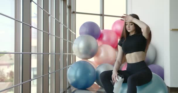 Woman with water sitting on fit ball in gym — Wideo stockowe