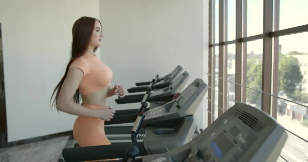 Mujer joven corriendo en la cinta de correr en el gimnasio — Vídeo de stock