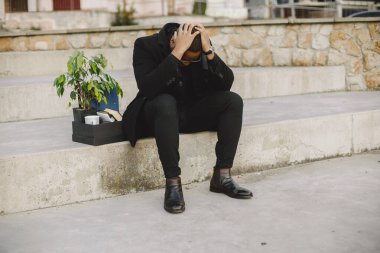 Frustrated black fired man itting outside with box