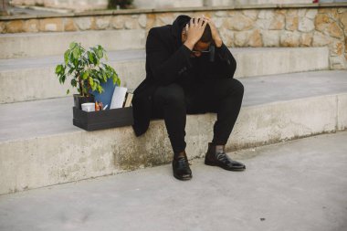 Frustrated black fired man itting outside with box