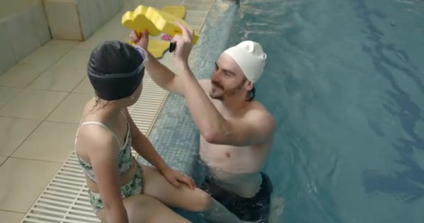 Coach puting op reddingvest op een meisje in een zwembad — Stockvideo