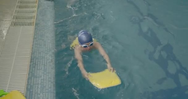 Девочка учится плавать в бассейне с доской — стоковое видео