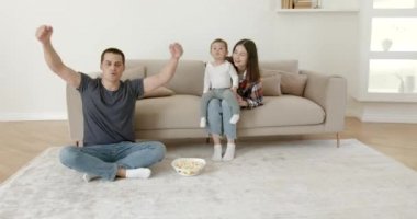 Kanepede çocuklu genç bir aile televizyon izliyor.