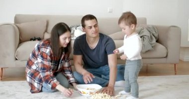 Çocuk, ebeveynlerine kaseye patlamış mısır koymalarında yardım ediyor.