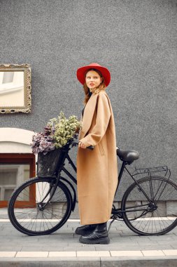 Bisikletinin yanında duran kırmızı şapkalı kız içinde sepet ve çiçeklerle.