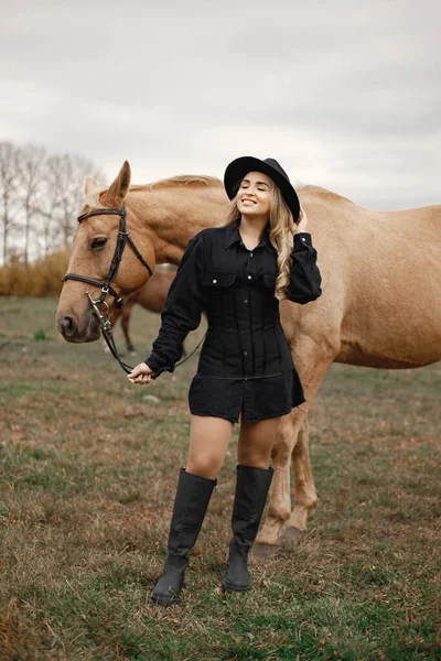 Krásná blondýnka s blond vlasy a hnědý kůň v terénu — Stock fotografie