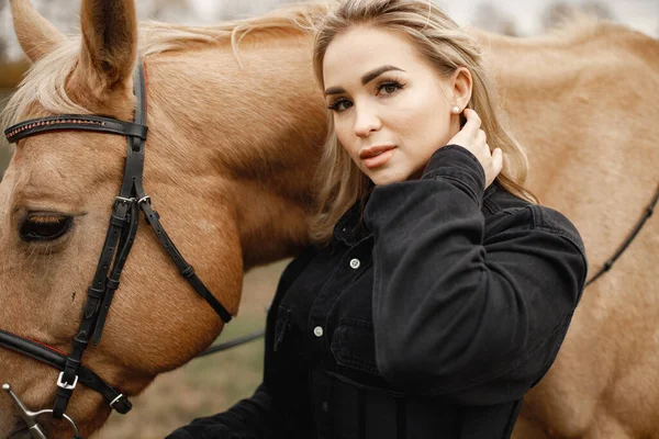 Mooie blonde vrouw met blond haar en een bruin paard in het veld — Stockfoto