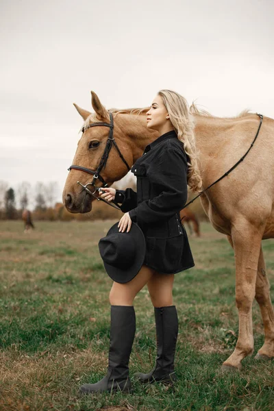 Schöne blonde Frau mit blonden Haaren und einem braunen Pferd auf dem Feld — Stockfoto
