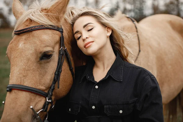 Mooie blonde vrouw met blond haar en een bruin paard in het veld — Stockfoto