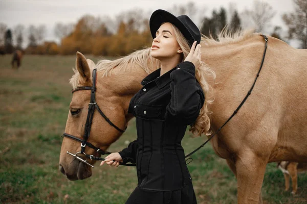 Mooie blonde vrouw met blond haar en een bruin paard in het veld — Stockfoto