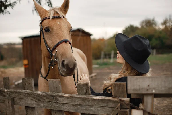 農場のフェンスの後ろに茶色の馬に触れる女性 — ストック写真