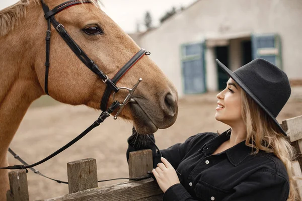 Vrouw die een bruin paard aanraakt achter het hek op een boerderij — Stockfoto