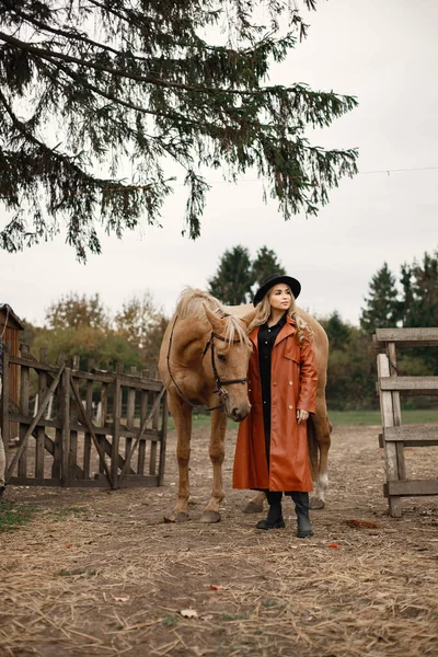 Vrouw in rode leren jas raakt een bruin paard aan op een boerderij — Stockfoto