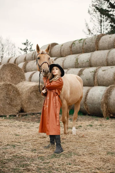 Vrouw in rode leren jas raakt een bruin paard aan op een boerderij — Stockfoto