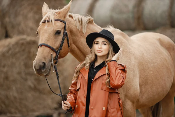 Жінка в червоному шкіряному пальто торкається коричневого коня на фермі — стокове фото
