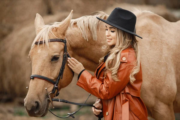Femme en manteau de cuir rouge touchant un cheval brun sur une ferme — Photo